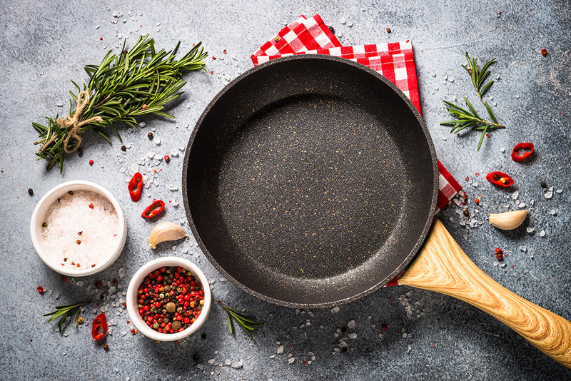 An empty frying pan alongside herbs, spices, and seasonings