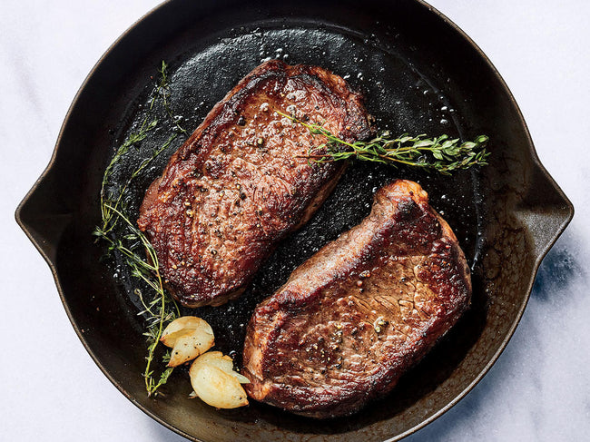 Two well-done steaks in a pan with garlic and sage